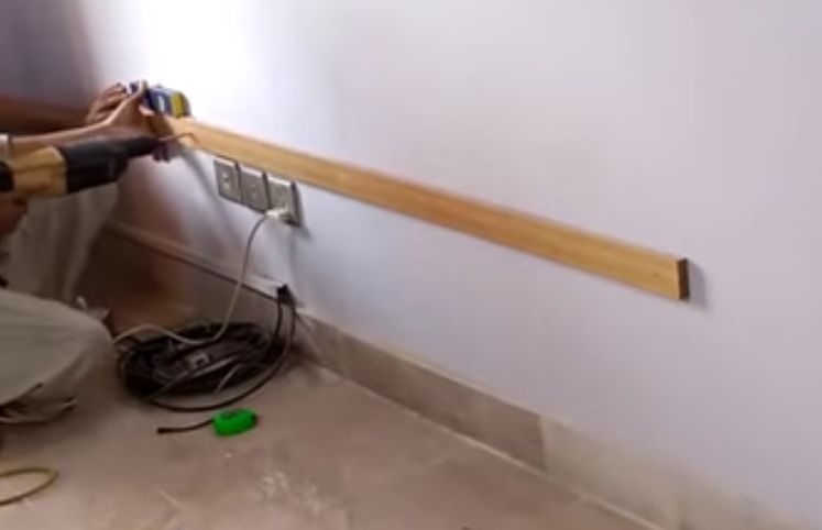 A man is mounting a TV on the wall with a drill while trying to hide wires