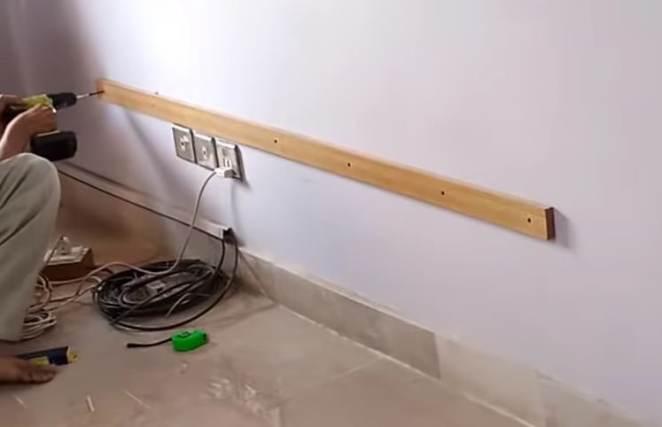 A man is working on a wall with a drill to hide wires on a wall-mounted TV