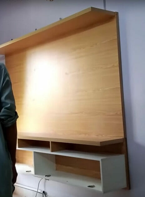 A man demonstrating how to hide wires on a wall-mounted TV using a wooden tv stand