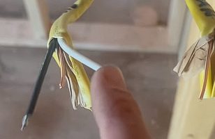 A person checking a stripped and scraped yellow wire