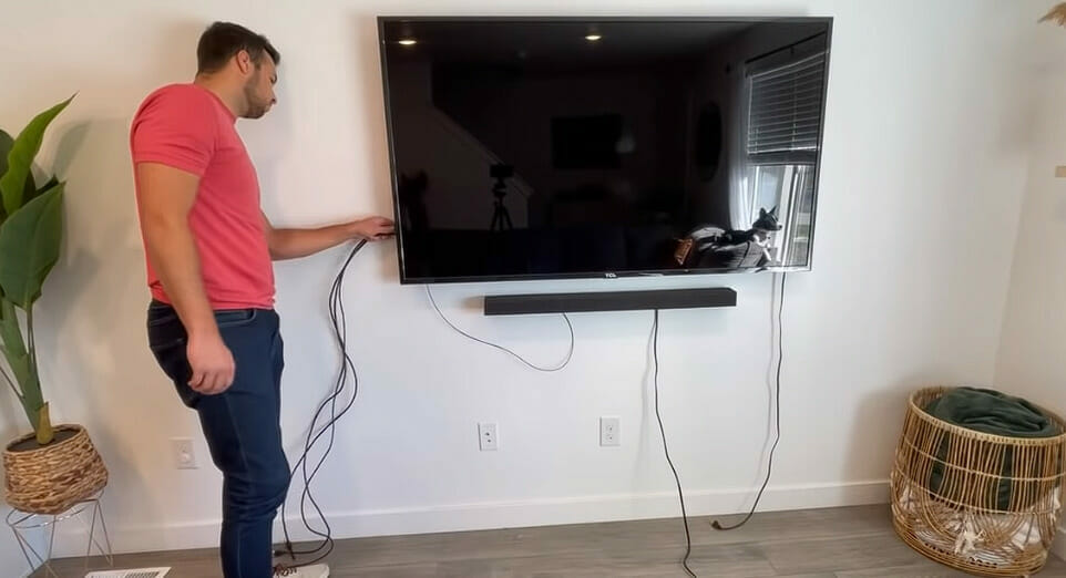 A man standing beside a mounted tv and fixing the wires