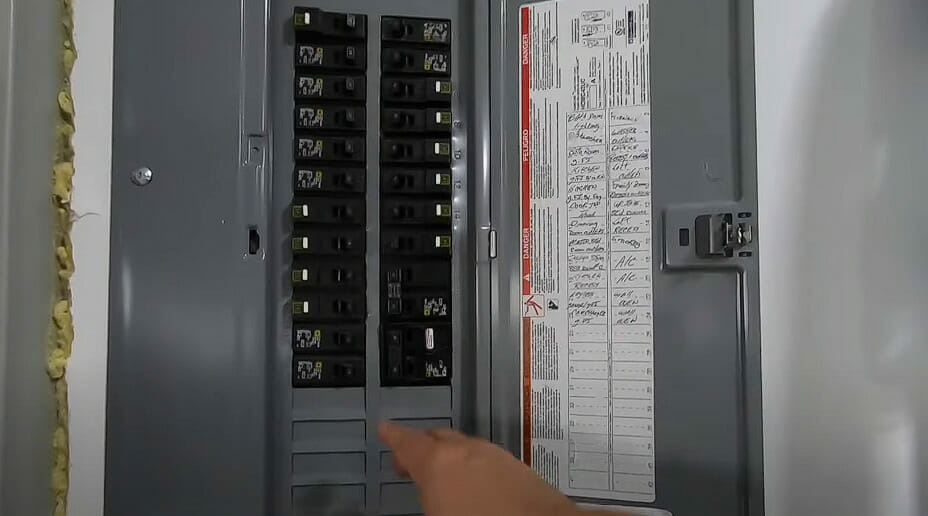 A person pointing on an open main circuit panel on the wall