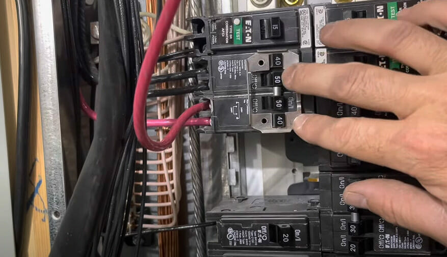 A person inserting a GFCI breaker into an open slot of a panel