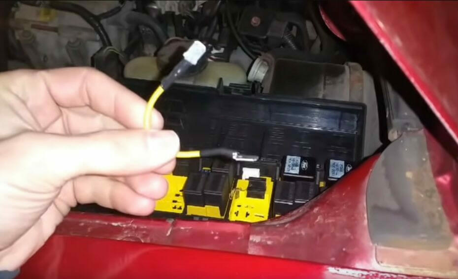 A person is connecting a yellow wire to directly power the fuel pump from the car's battery