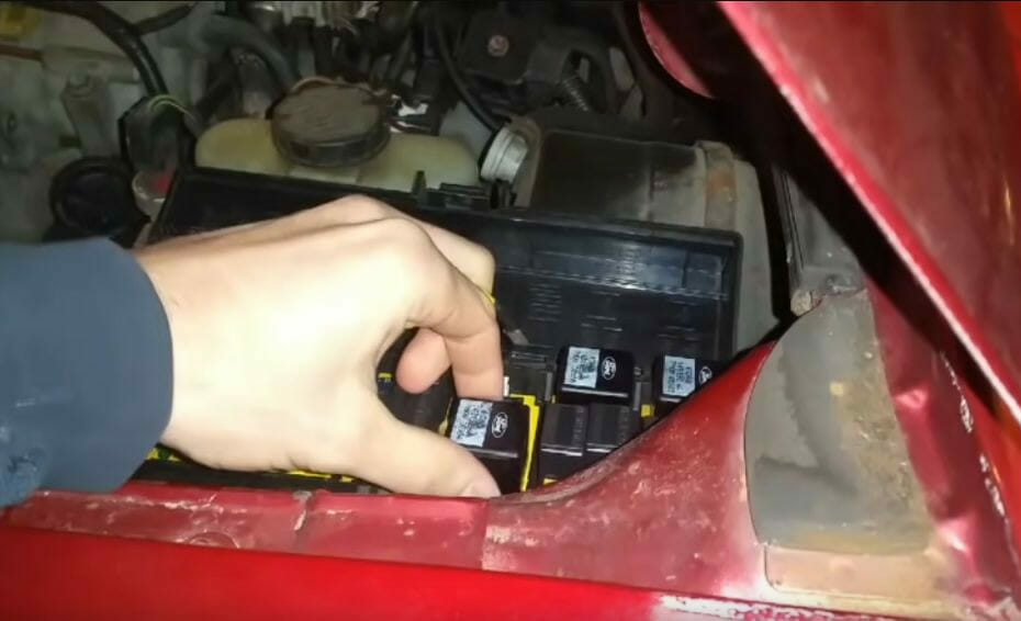 A person is removing a relay in a red car