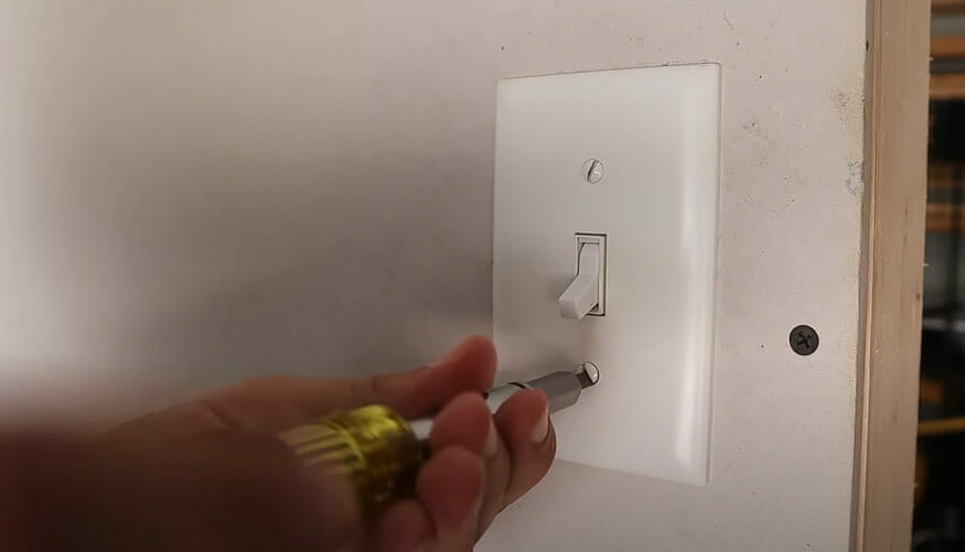 A man unscrewing the light switch on the wall