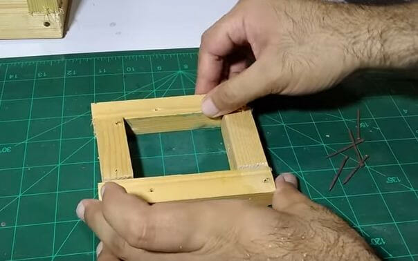 A man making the door frame of a bird's cage