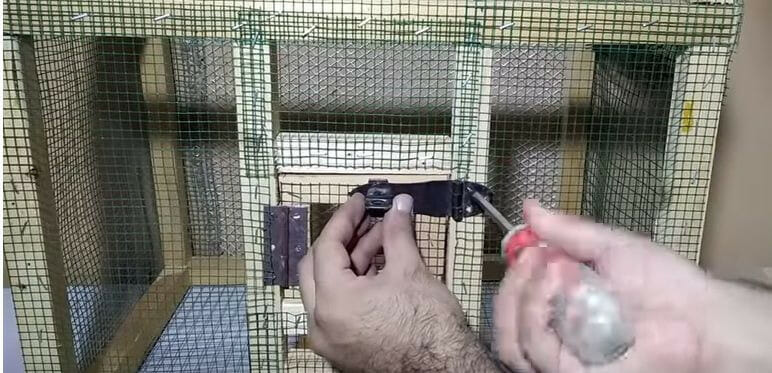 A man attaching a latch to the door of a bird's cage