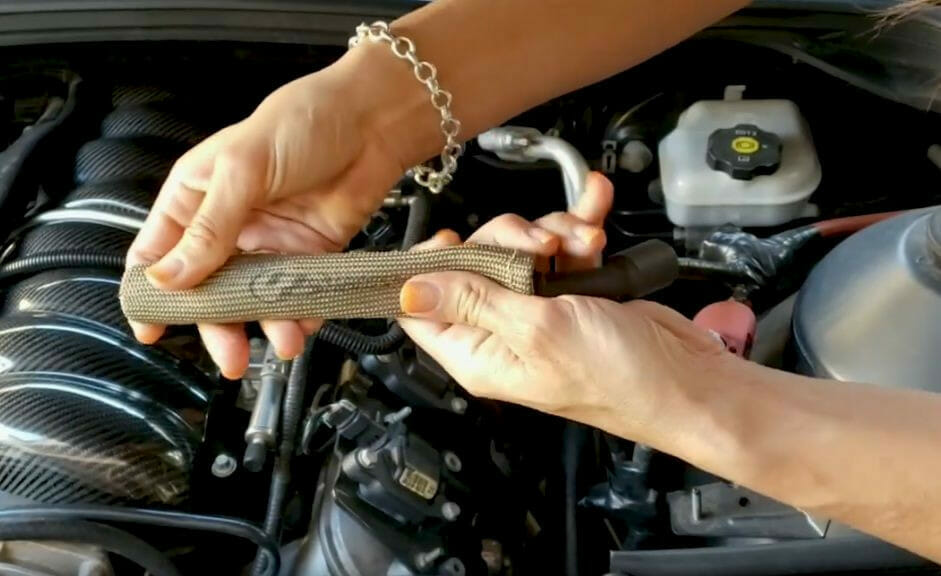 A person is installing spark plug wire heat shields on a car engine