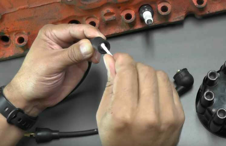 A person is installing spark plug wire heat shields in a car engine