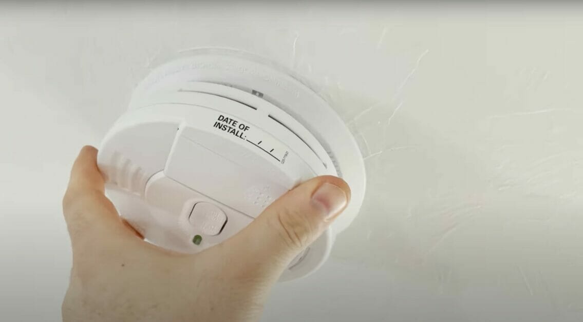 man installing smoke detector into a white ceiling