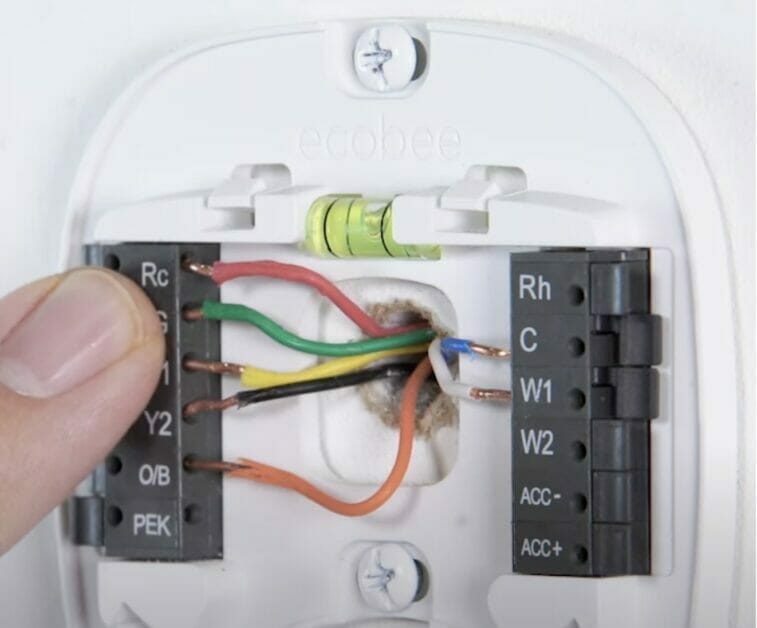 A person is installing wires in a thermostat, including the RC wire