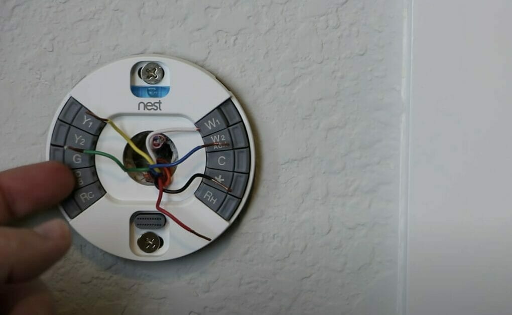A person is installing a wire for a thermostat on a wall.