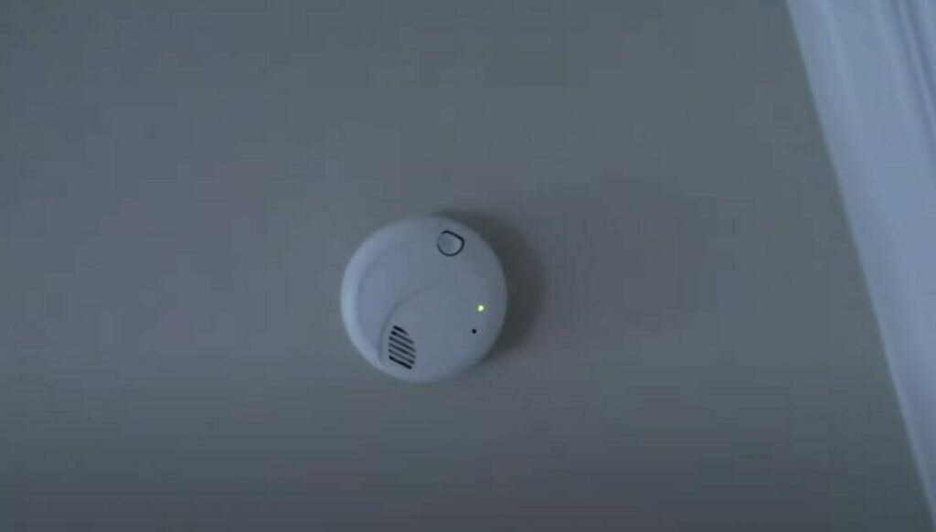 A hard-wired smoke detector at the ceiling showing green light