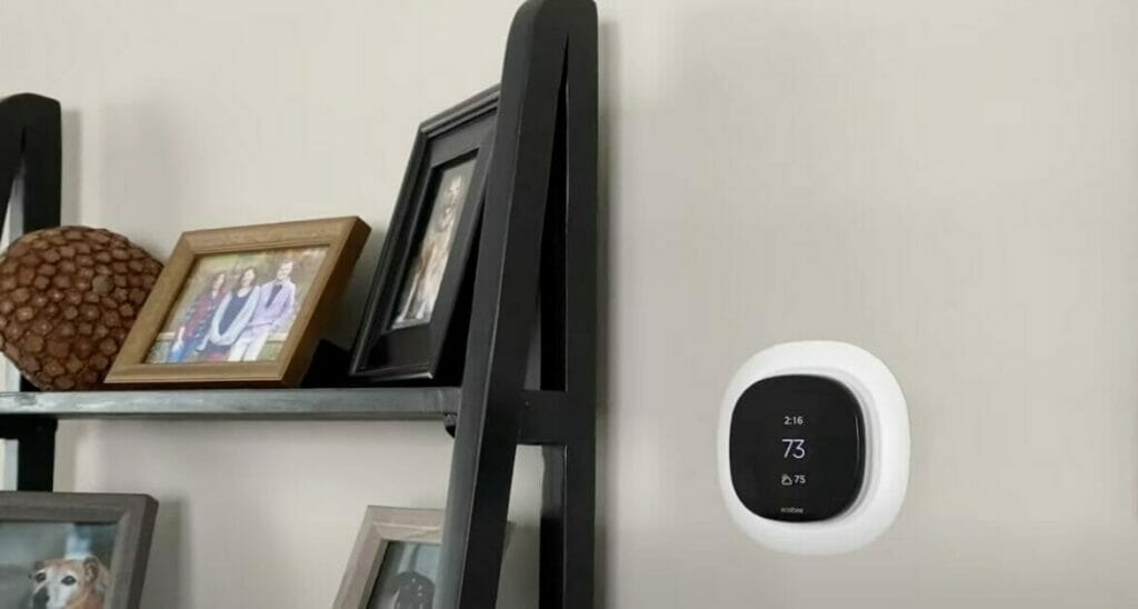 A thermostat is mounted on a wall in a living room besides a rack of picture frames