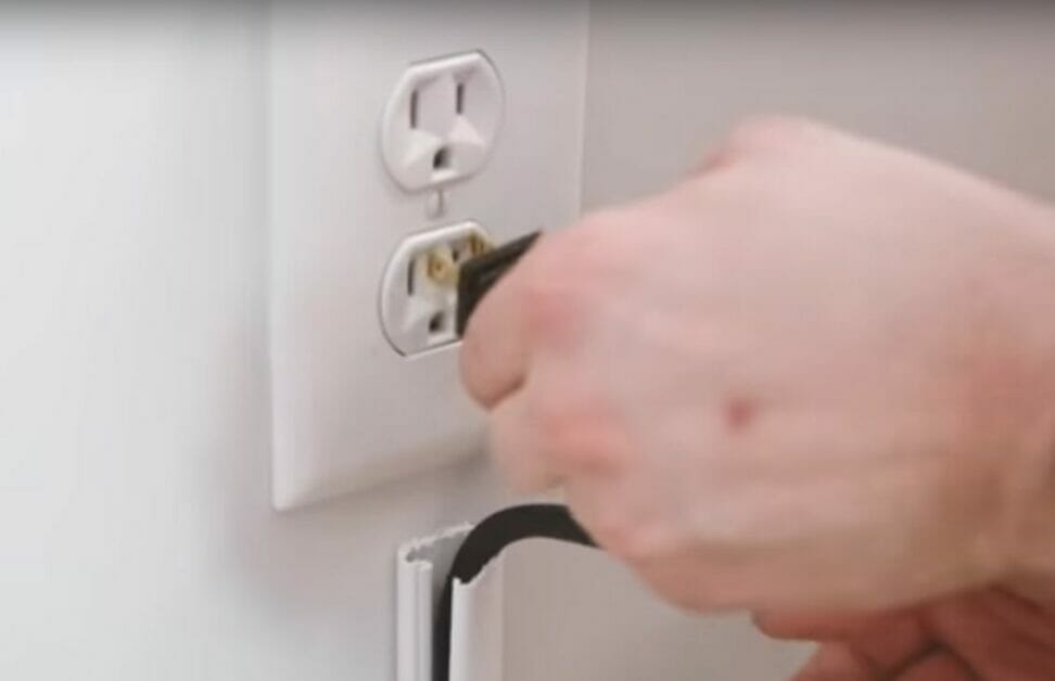 A person is concealing wires while plugging into a wall outlet