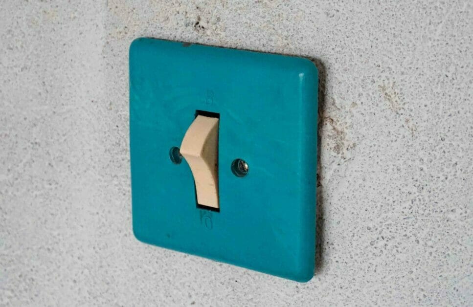 A single switch with emerald green cover mounted on a rough wall