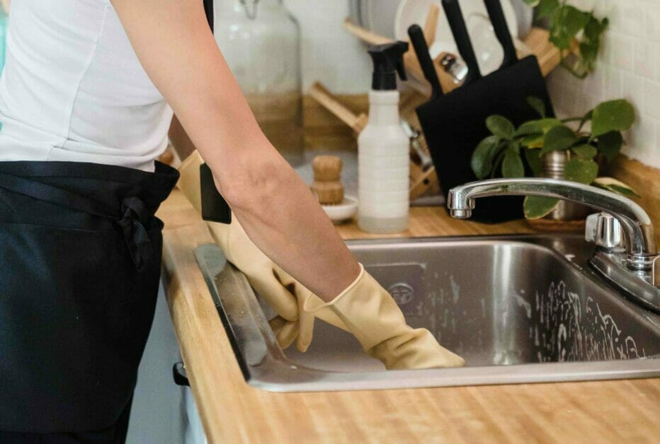 A woman with gloves cleaning the kitchen sink