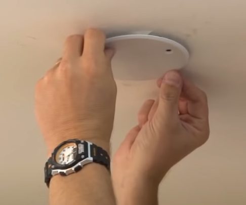 A person installing a blank cover plate on the ceiling for a smoke detector