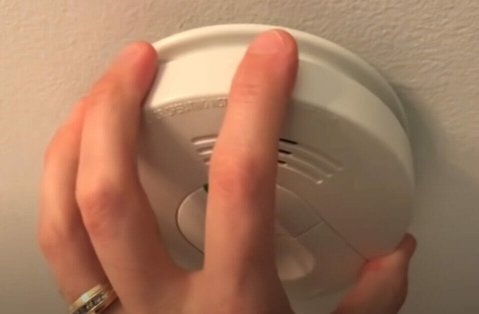 A person removing the cover of a smoke detector