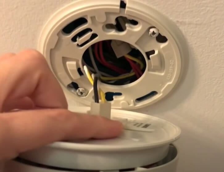 A person disconnecting the wires of a smoke detector