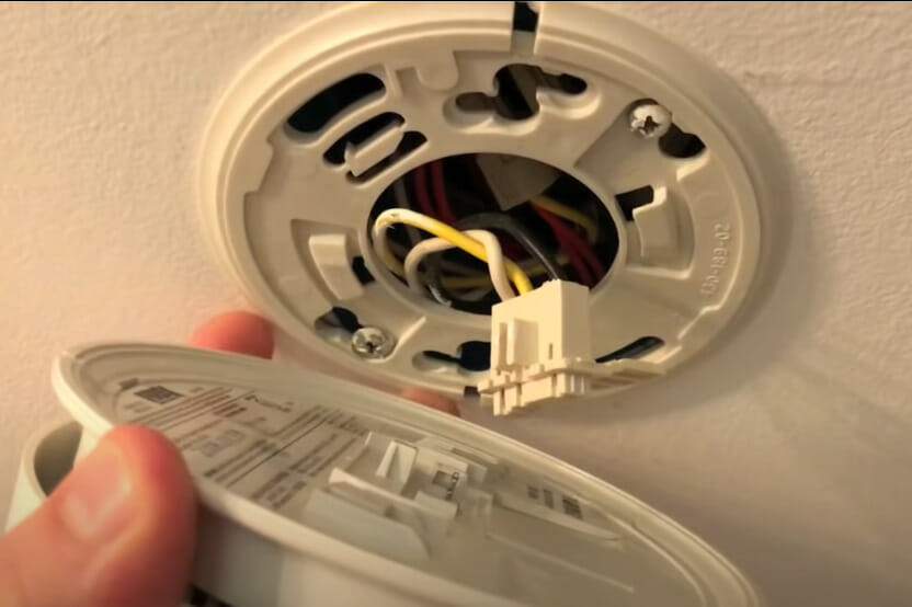 A person detaching the cover of a smoke detector in the ceiling