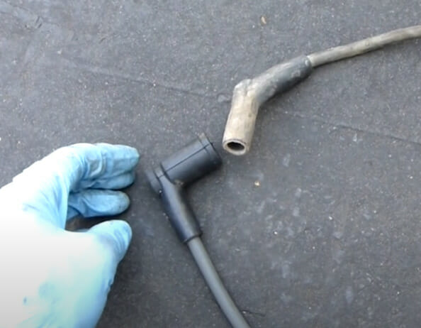 A person hand with blue gloves besides two spark plug wires on the ground