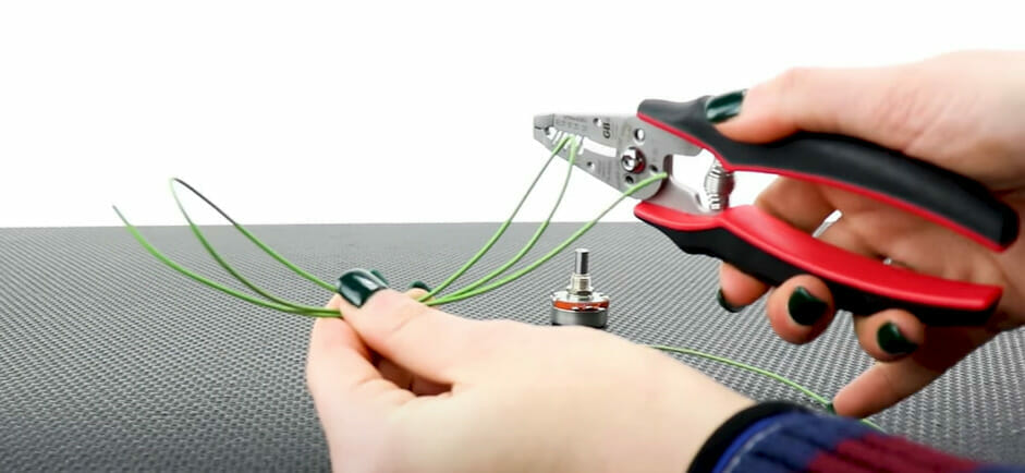 A woman is soldering the ends of a green wire to connect to a potentiometer