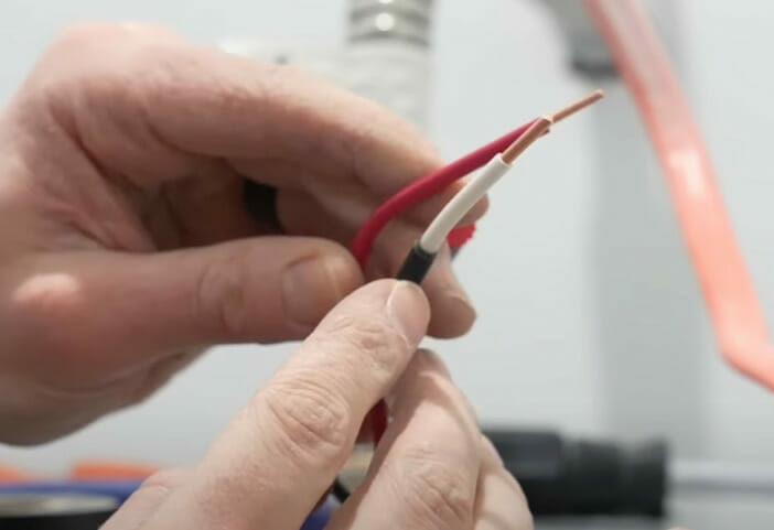 A person connecting wires to the red lead of a water heater
