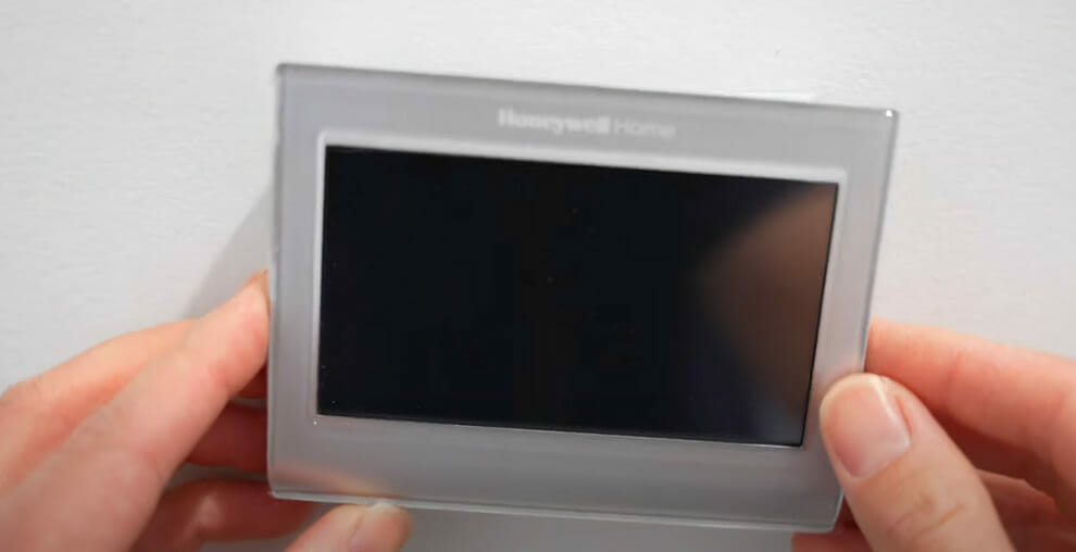 A person holding a Honeywell thermostat