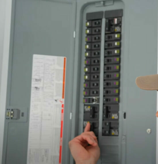 A man is turning back on a circuit breaker in a main circuit panel