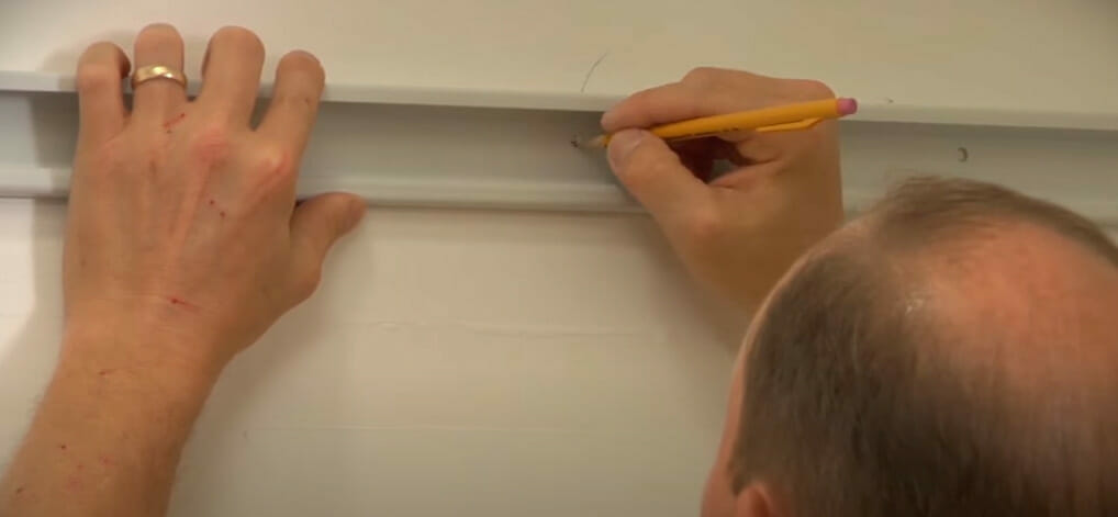 A man is using a pencil to mark where to attach a bracket for wire shelves