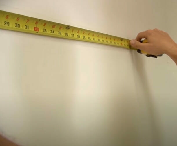 A person measuring a wall for wire shelves