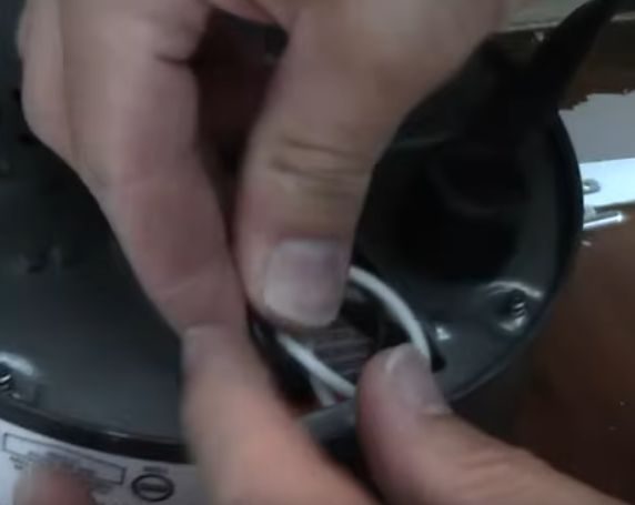 A person tucking the wires inside the compartment of a garbage disposal