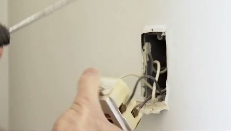 A man using a screwdriver to open an outlet