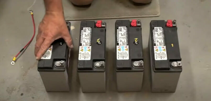 A person is arranging four batteries in series on a floor