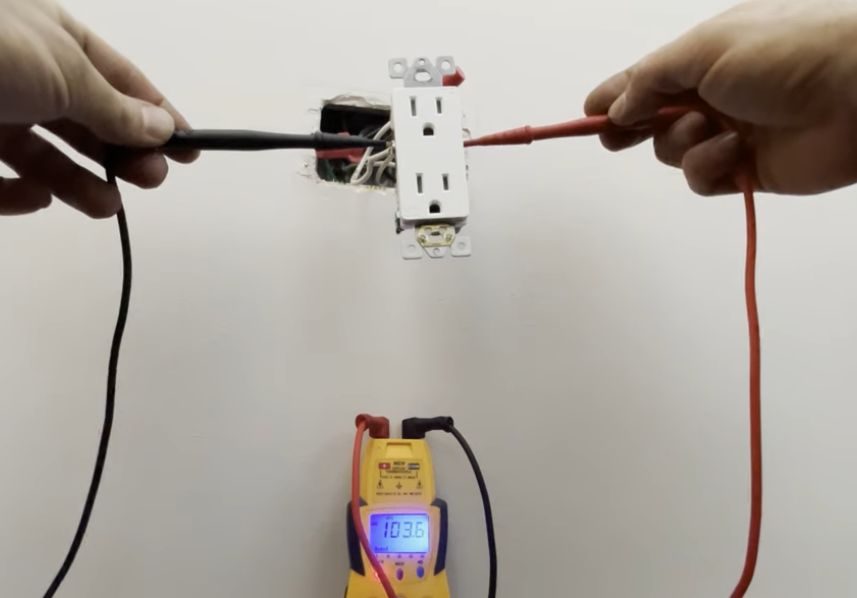 A person holding a multimeter probe to test the outlet on the wall