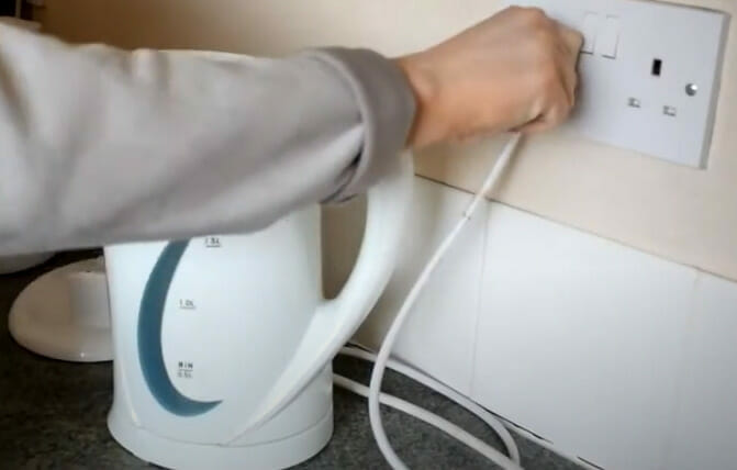 A person plugging an electric kettle into an outlet