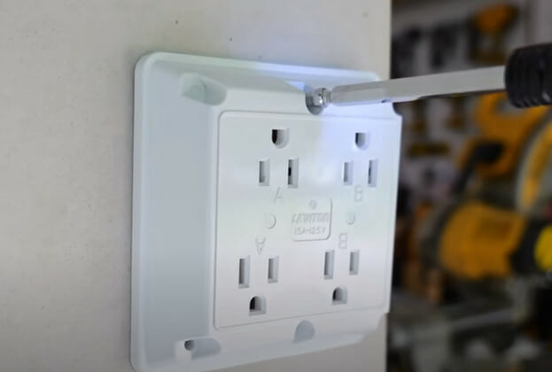 A person screwing the double outlet mounted on the wall