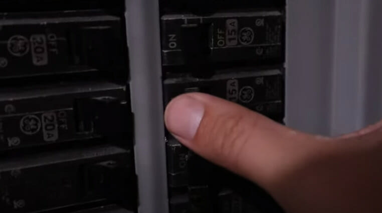 A person turning on a circuit breaker in a main circuit panel