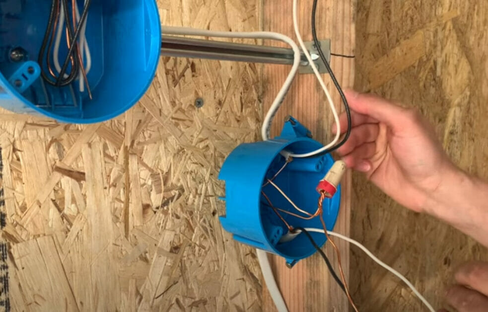 A person is installing a blue electrical box with wires