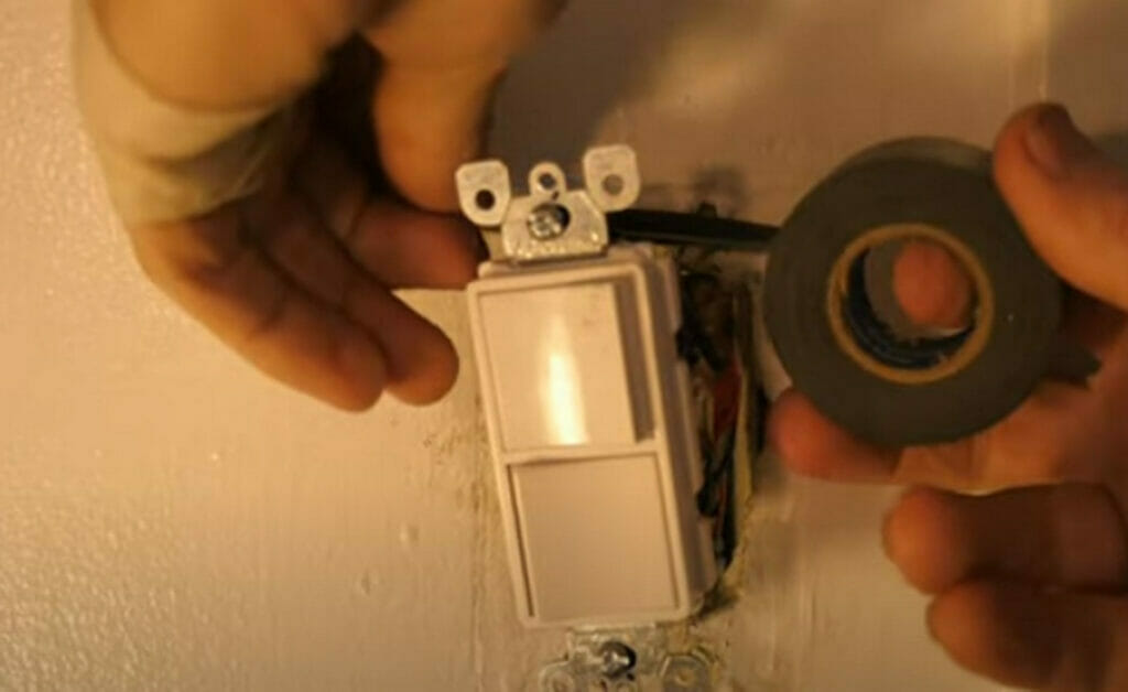 A person wrapping the double switch with an electric tape