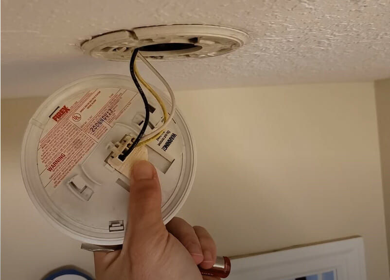 A person opening the cover of a smoke detector mounted at the ceiling
