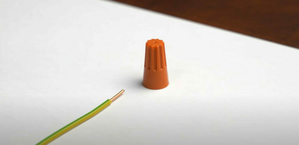 A green-yellow stripe wire with an orange wire nut on the table