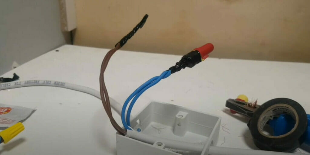 A wire is connected to a light switch on a table and electrical tape and a wire nut on the end