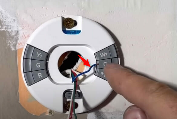 A person pointing on the C-wire of a thermostat