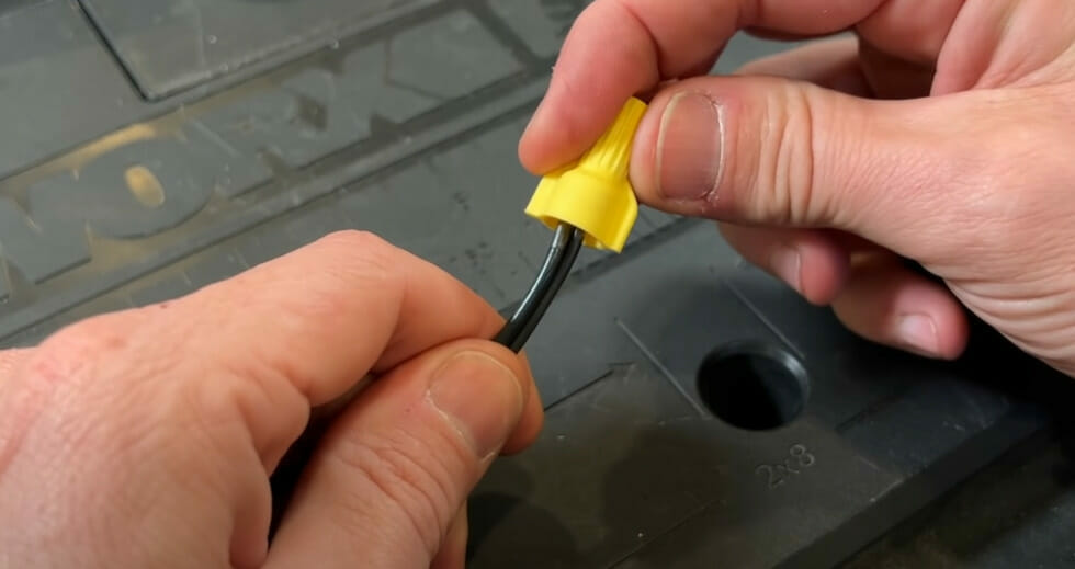 A person is using a yellow wire nut to cap off a wire