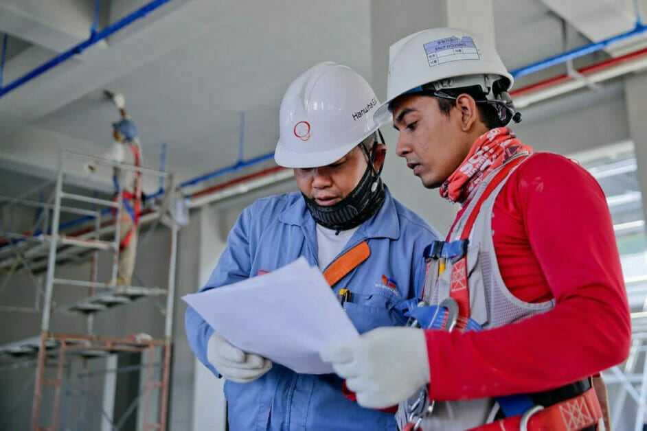 Two construction workers discussing electrical with a document in hand