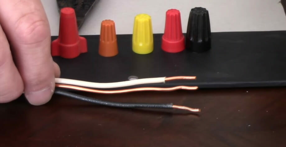 A person holding a black, brown, and white wires with 5 wire caps in different colors