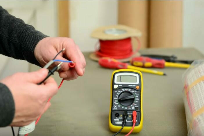 A man uses a multimeter to test a wire in a heated floor